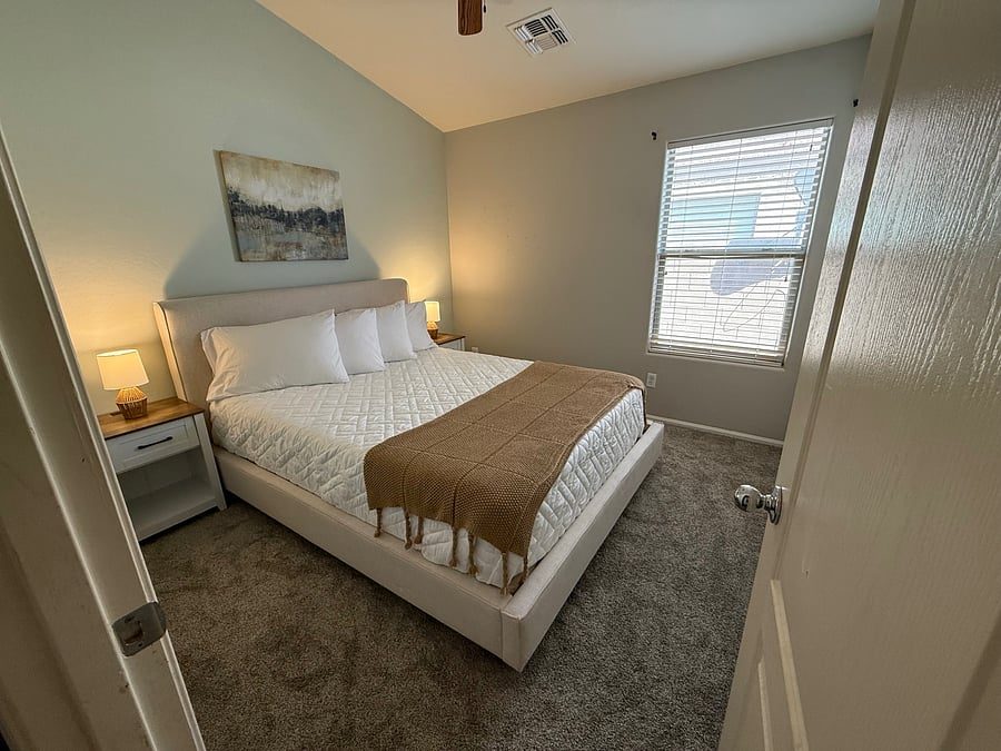 Furnished bedroom with made bed and nightstand lamps in the Maricopa, AZ rental house